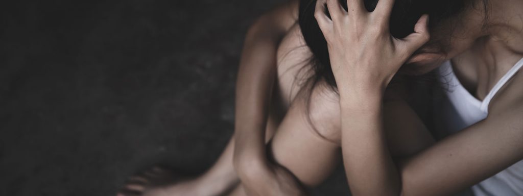 Woman sitting on the floor with her head down and hands in her hair, appearing distressed or overwhelmed in a dark, shadowy environment.